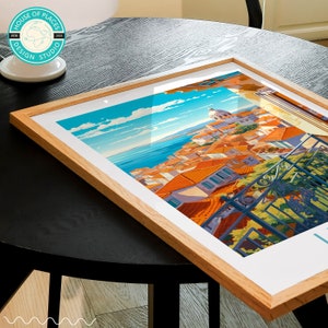 May include: A framed print of a colorful illustration of a cityscape with a blue sky and ocean in the background. The city is built on a hillside and has many red-tiled roofs. The print is in a wooden frame.