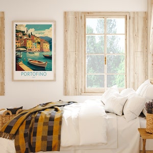 May include: A framed print of a colorful illustration of the Italian town of Portofino, with boats in the water. The print is hanging on a white wall above a bed with white bedding and a yellow and black plaid throw blanket.