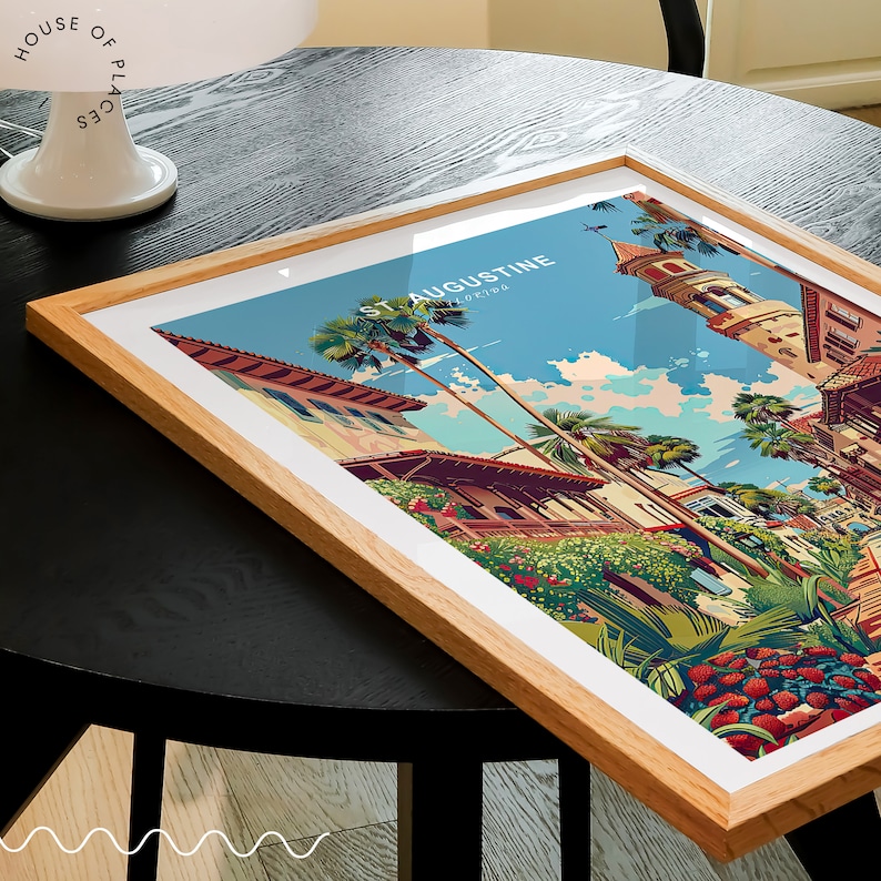 May include: A framed print of a colorful illustration of St. Augustine, Florida. The illustration depicts a street scene with palm trees, buildings, and a blue sky.