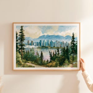 May include: A framed landscape print featuring a watercolour-style city skyline across a body of water, framed by tall evergreen trees in the foreground and distant blue mountains under a soft, cloudy sky with light blue and cream tones.