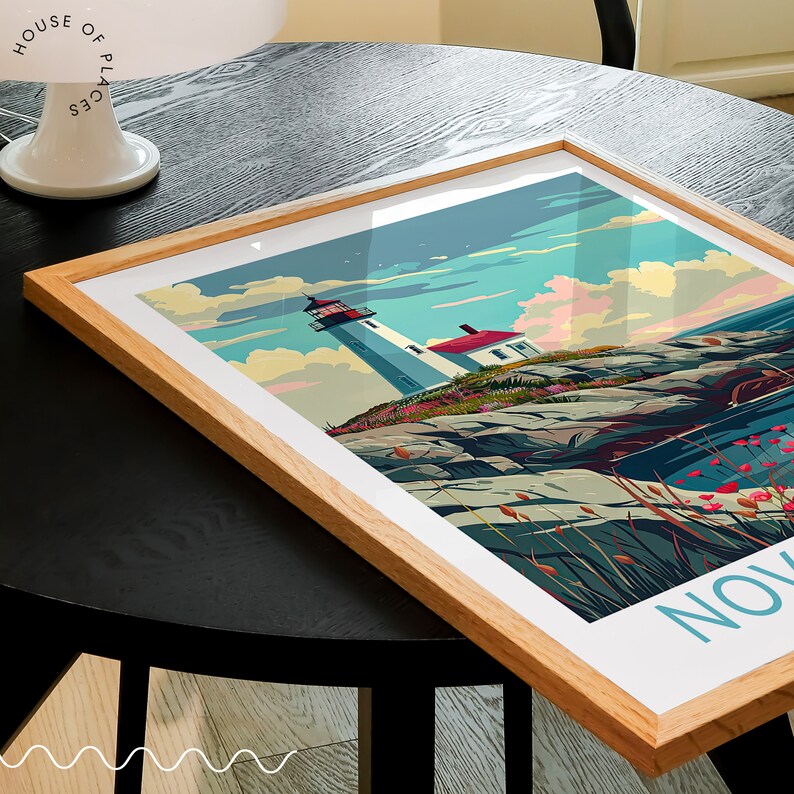 K&ouml;nnte beinhalten: Gerahmter Kunstdruck mit einer K&uuml;stenlandschaft mit Leuchtturm. Das Kunstwerk zeigt einen wei&szlig;en Leuchtturm mit roter Spitze vor einem blauen Himmel mit Wolken. Der Druck ist in einem hellen Holzrahmen.