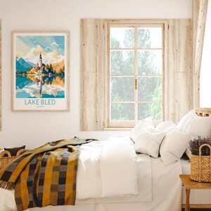 Op de afbeelding: Een wit bed met een geel en zwart geruit deken, witte kussens en een rieten mand met lavendelbloemen op een houten nachtkastje. Een ingelijst afdruk van het meer van Bled, Sloveni&euml;, hangt aan de muur boven het bed.