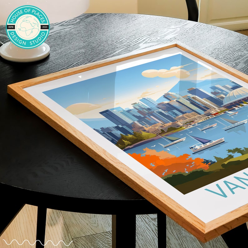 May include: A framed print of a colourful illustration of the Vancouver skyline with boats in the water and a green park in the foreground. The print has a white background and a light blue border. The text "VAN" is visible in the bottom right corner.