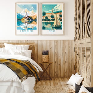 Op de afbeelding: Twee ingelijste reisposters met illustraties van het meer van Bled in Sloveni&euml; en Split in Kroati&euml;. De posters hangen aan een houten lambrisering in een slaapkamer.