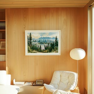 May include: A framed landscape painting featuring a city skyline across a body of water, framed by tall evergreen trees in the foreground and distant blue mountains under a cloudy sky, displayed on a light-coloured wood panelled wall.