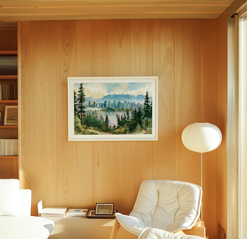 May include: A framed landscape painting featuring a city skyline across a body of water, framed by tall evergreen trees in the foreground and distant blue mountains under a cloudy sky, displayed on a light-coloured wood panelled wall.