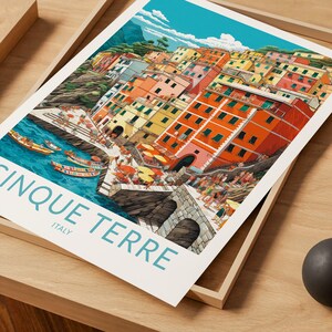 K&ouml;nnte beinhalten: Eine farbenfrohe Illustration des italienischen Dorfes Cinque Terre mit bunten H&auml;usern, die in den Hang gebaut sind und auf eine t&uuml;rkisblaue Bucht mit Booten blicken. Der Text "Cinque Terre" und "Italien" ist unter dem Bild gedruckt.