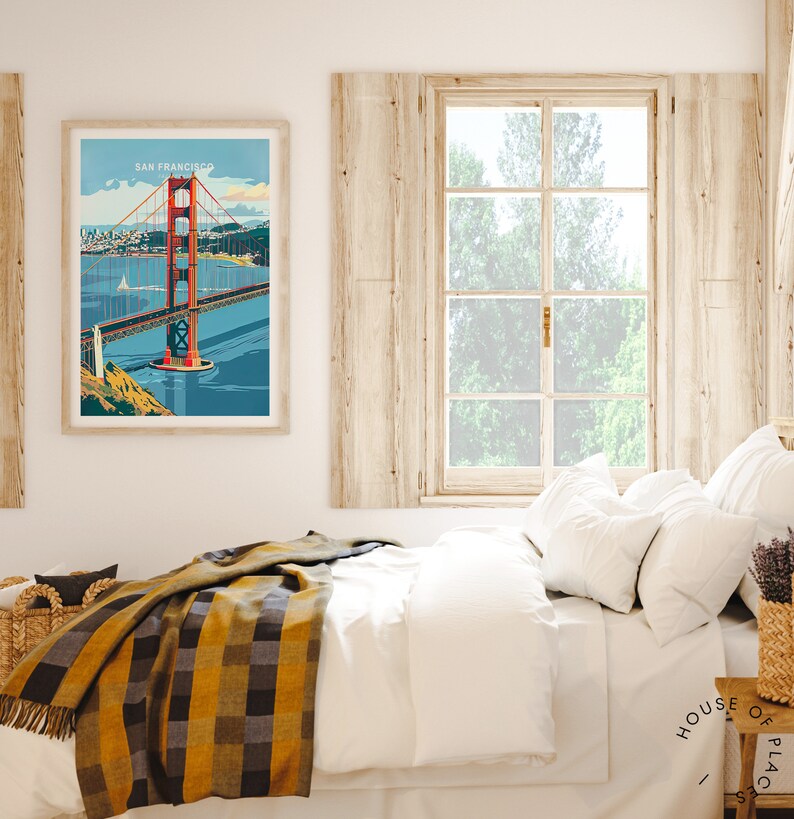 May include: A framed poster featuring a vintage illustration of the Golden Gate Bridge in San Francisco, California. The poster is hanging on a white wall above a bed with a white duvet and a yellow and black checked throw blanket.