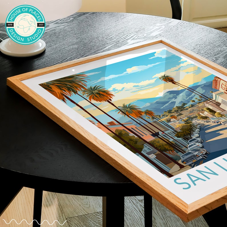 May include: A framed print of a colourful illustration of a street scene in San Luis Obispo, California. The print features palm trees, buildings, and cars. The text "SAN LUIS OBISPO" is printed in blue at the bottom of the print.