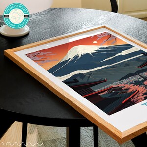 Pu&ograve; includere: Una stampa incorniciata del Monte Fuji, una famosa montagna giapponese, con un cielo rosso e fiori di ciliegio in primo piano. La stampa &egrave; in una cornice di legno e ha il testo "House of Places Design Studio" in un cerchio in basso.