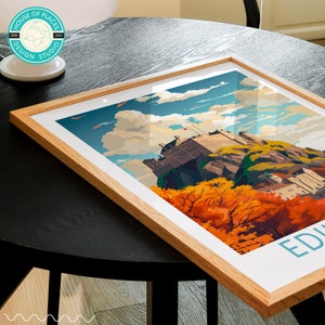 May include: A framed print of Edinburgh Castle in Scotland. The castle is perched on a rocky hilltop with a backdrop of blue sky and fluffy white clouds. The print features a vibrant color palette with autumnal foliage in shades of orange, yellow, and red.