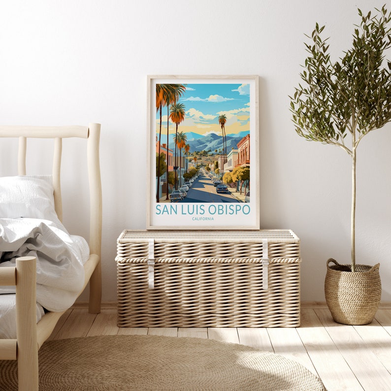 May include: A framed poster featuring a colourful illustration of a street scene in San Luis Obispo, California. The poster depicts a blue sky with white clouds, palm trees, and buildings. The text on the poster reads "San Luis Obispo, California".