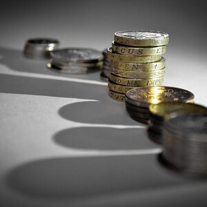 Puede incluir: Una pila de monedas de libra esterlina británicas, con la inscripción "DECUS ET TUTAMEN" visible en la moneda superior, se encuentra sobre una superficie blanca con una sombra detrás.