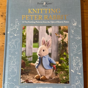 May include: A light blue hardback book titled Knitting Peter Rabbit, 12 Toy Knitting Patterns from the Tales of Beatrix Potter by Claire Garland. The cover features a knitted rabbit in a blue jacket and white line art of various characters.