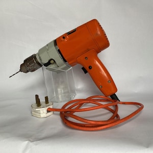 May include: An orange and white electric drill with a black power cord and a white plug. The drill is on a clear plastic stand.