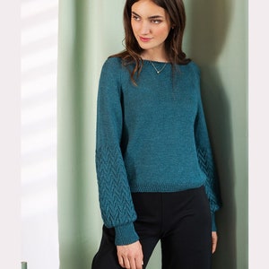 Peut inclure: Un pull en tricot bleu sarcelle avec un col bateau et un motif en tricot torsadé sur les manches.