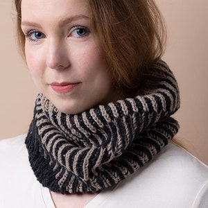 May include: A woman wearing a black and brown striped knit cowl neck scarf. The scarf is made of a soft, textured yarn and has a simple, elegant design.