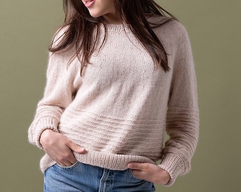 Può includere: Una donna indossa un maglione di lana beige chiaro con una vestibilità leggermente morbida e maniche lunghe. Indossa jeans blu e ha le mani in tasca.