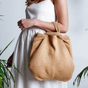May include: A woman in a white dress is holding a large, brown, knitted tote bag.