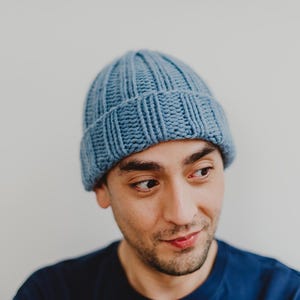 May include: A person wearing a blue knitted beanie hat. The hat has a ribbed texture and a folded brim.