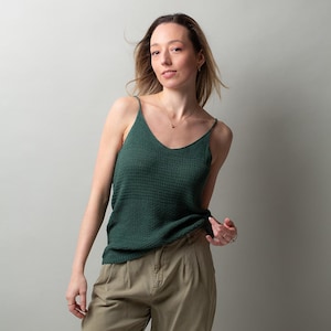 Könnte beinhalten: Eine Frau trägt ein grünes Tanktop und eine Khakihose. Sie steht vor einem hellgrauen Hintergrund.