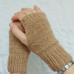 以下が含まれることがあります： 茶色の指なしニット手袋のペア。手袋は柔らかく暖かい素材で作られており、冬の寒さから手を守るのに最適です。