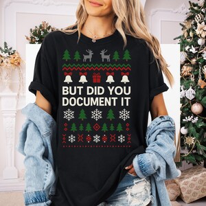 Peut inclure: T-shirt noir avec un motif de pull de Noël. Le motif comprend des sapins verts, des rennes gris, des nœuds rouges, des cloches blanches et des flocons de neige. Le texte "BUT DID YOU DOCUMENT IT" est au centre.