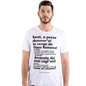 Può includere: Maglietta bianca con testo nero che dice "Senti, a pezzo demmer*a! lo vengo da Fiano Romano! Avvocato dei miei cogl'oni! Come mi chiamo?"
