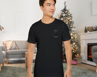 May include: Black crew neck t-shirt with the text "MERRY GOTHMAS" in a gothic font. The shirt is made of a soft material and is suitable for casual wear. The design is located on the upper left chest area.