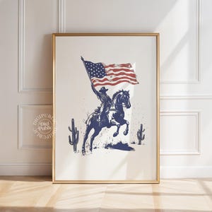 A vintage-style illustration of a cowboy on horseback waving an American flag, flanked by two cacti — perfect for rustic western or patriotic-themed decor.