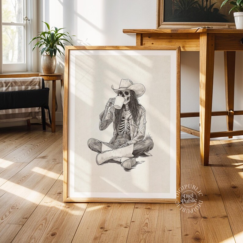 May include: Black and white illustration of a skeleton wearing a cowboy hat and denim jacket, seated cross-legged and drinking from a mug. The artwork is framed in a wooden frame and is displayed in a room with wooden floors.