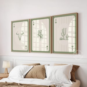 Puede incluir: Tres impresiones artísticas enmarcadas con temática del Salvaje Oeste, cada una representando una carta de As. Las ilustraciones incluyen una calavera de toro, un vaquero a caballo y un cactus. Los marcos tienen un borde verde y un acabado de madera clara.