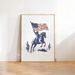 A vintage-style illustration of a cowboy on horseback waving an American flag, flanked by two cacti — perfect for rustic western or patriotic-themed decor.