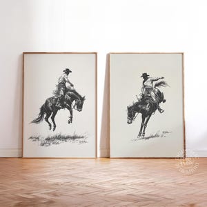 May include: Two framed black and white prints showing a cowboy riding a bucking bronco. The cowboy wears a hat and riding gear. The artwork is set against a cream background, with a wooden frame.