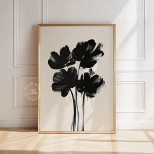 May include: A framed art print featuring a minimalist floral design. Bold black brushstrokes depict four stylized flowers against a neutral background. The artwork is encased in a gold-colored frame, adding a touch of elegance.