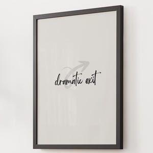 May include: A framed art print featuring the words "dramatic exit" in a handwritten style. The print has a light grey background and a black frame. An arrow graphic is above the text.