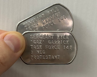 May include: Two silver military dog tags with the text "SERGEANT KYLE GAZ GARRICK TASK FORCE 141 B NEG PROTESTANT".