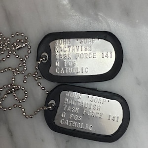 May include: Two silver dog tags with black rubber coating. The tags have the text "JOHN 'SOAP' MACTAVISH TASK FORCE 141 O POS CATHOLIC" engraved on them.