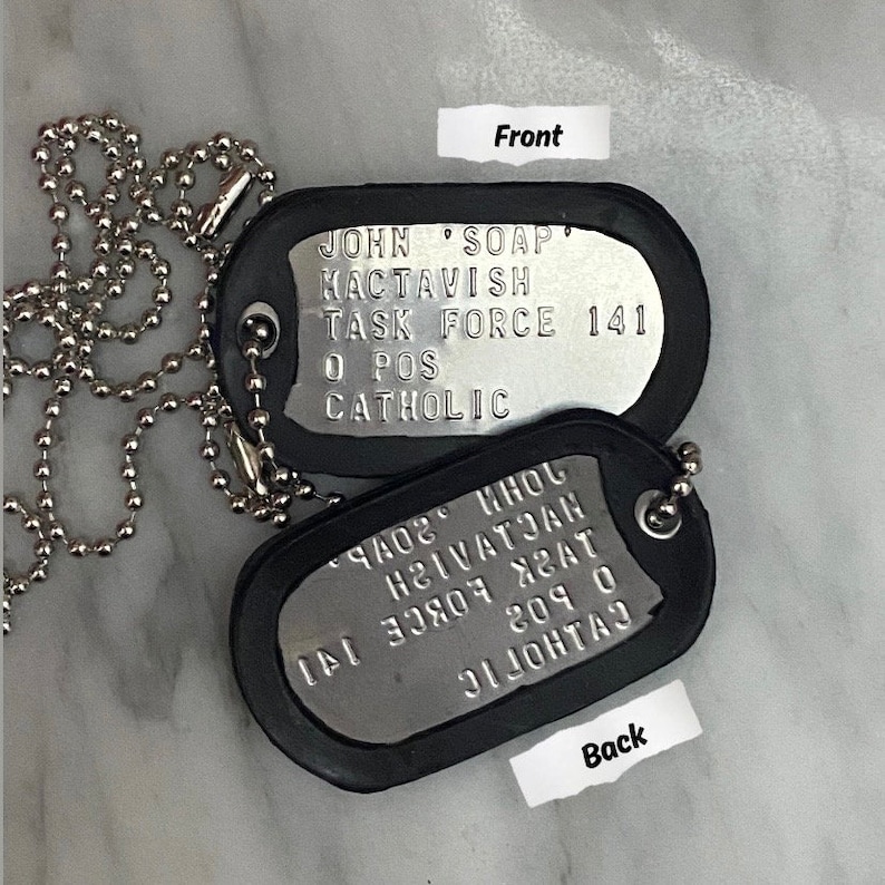 May include: Two black metal dog tags with a silver chain. The front tag reads "JOHN 'SOAP' MACTAVISH TASK FORCE 141 O POS CATHOLIC". The back tag reads "ЧАОГ ИНOL HEIVATIAN ДУСК LОВСЕ 141 १०१ ० СУДНОГІС".