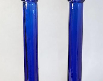 May include: A pair of cobalt blue glass candle holders with a flared base and a cylindrical body.