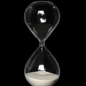 May include: A clear glass hourglass featuring a rounded bulb shape with a narrow center neck. The bottom bulb is filled with fine white sand, while the top bulb is empty. The glass surface reflects light, creating bright highlights against the black.