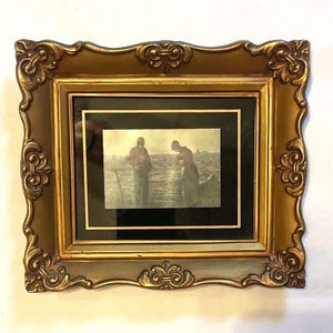 May include: A framed print featuring a sepia-toned image of two figures near water. The ornate gold-colored frame has decorative scrollwork. The print is set against a black matting.