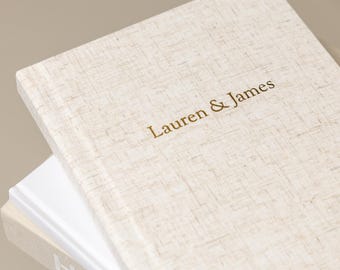 May include: A stack of three hardcover books. The top book has a textured, light beige cover with the gold text "Lauren & James." The second book has a white cover, and the bottom book has a beige cover with the partial text "HAU."