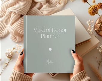 May include: A light gray planner with the text "Maid of Honor Planner" in white. A small white heart is below the text and the name "Madison" is written in cursive below the heart.