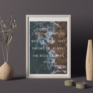 May include: A framed print with a quote about learning to embrace challenges. The quote reads "I have learned to kiss the wave that throws me against the rock of ages." The background image is an aerial view of ocean waves crashing against rocky shores.