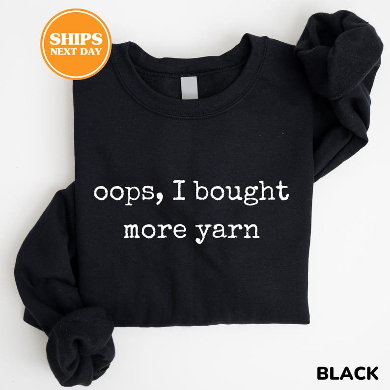 A black t-shirt with white text printed on it, which says "oops, I bought more yarn".