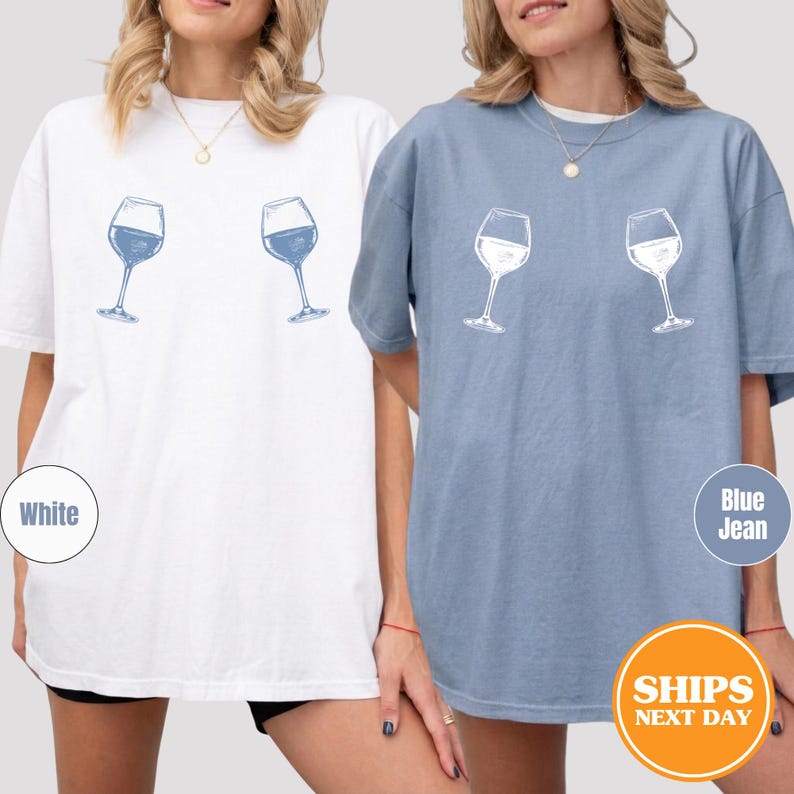 May include: Two t-shirts, one white and one blue, each featuring a wine glass graphic. The white shirt has a blue wine glass design, while the blue shirt has a white wine glass design. The shirts are casual and comfortable.