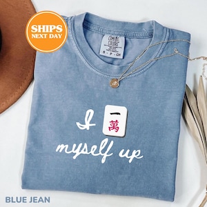 Pu&ograve; includere: Una maglietta blu jeans con la scritta "I 萬 myself up" in corsivo bianco. Una collana d'oro con un ciondolo &egrave; appoggiata sulla maglietta. La maglietta ha un'etichetta Comfort Colors.