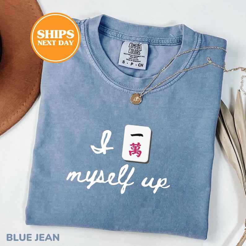 Pu&ograve; includere: Una maglietta blu jeans con la scritta "I 萬 myself up" in corsivo bianco. Una collana d'oro con un ciondolo &egrave; appoggiata sulla maglietta. La maglietta ha un'etichetta Comfort Colors.