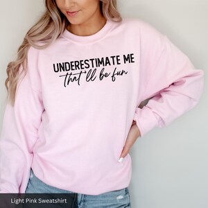 a woman wearing a pink sweatshirt that says, underestimate me that '